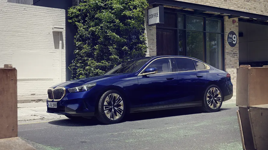 Blauer BMW 5er Limousine parkt vor einem Gebäude mit Pflanzenwand und Glasfront.
