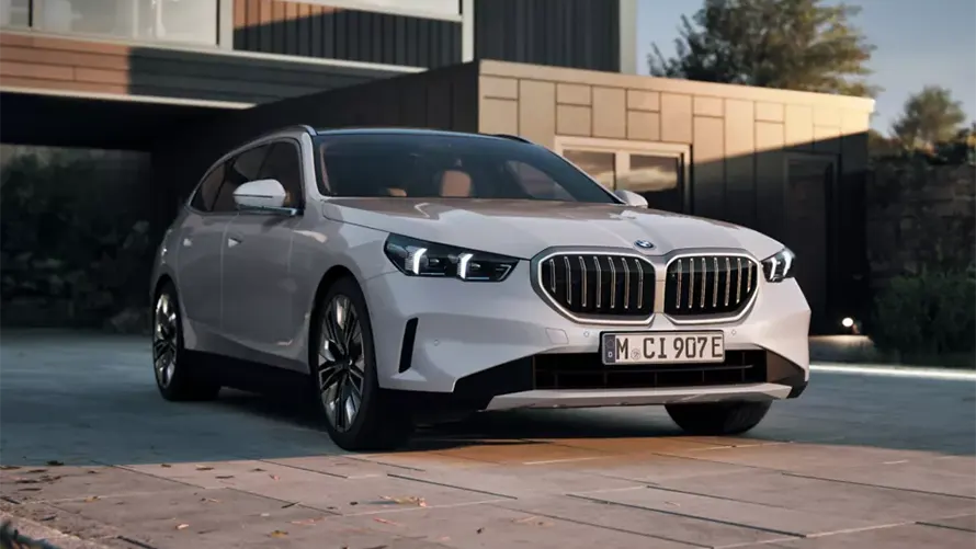 Silberner BMW auf einer Auffahrt vor einem modernen Gebäude bei Sonnenuntergang.