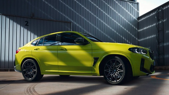 Leuchtgrüner BMW X4 M vor einer grauen Lagerhalle bei Tageslicht.