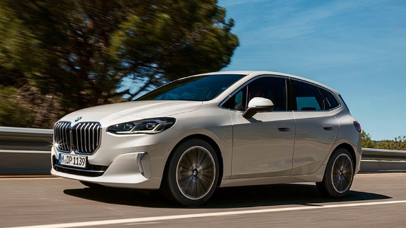 Silberner BMW 2er Active Tourer fährt auf einer Straße, umgeben von Bäumen unter blauem Himmel.