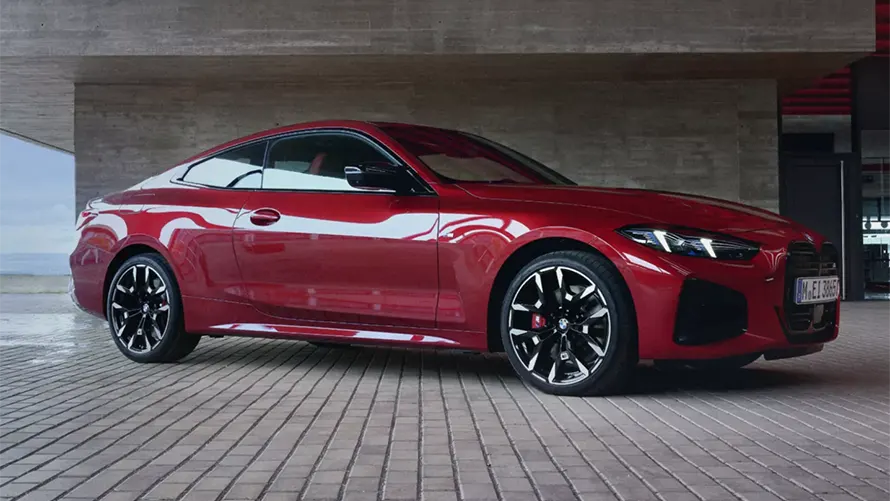 Rotes BMW 4er Coupé auf gepflasterter Fläche vor Betonwand, seitliche Ansicht.