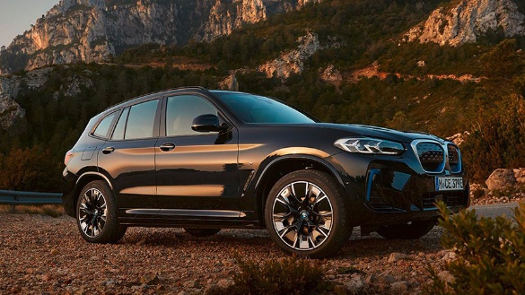 Schwarzer BMW iX3 steht auf einer Straße vor einer bergigen Landschaft bei Sonnenuntergang.