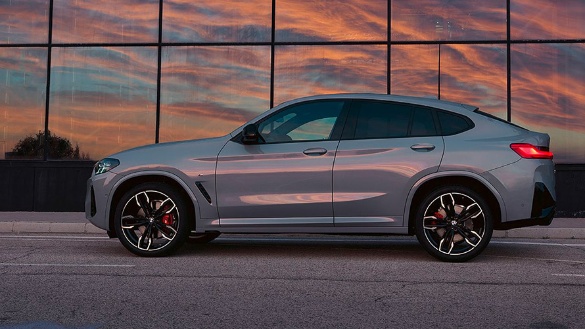 Silberner BMW X4 vor Glasfassade bei Sonnenuntergang.