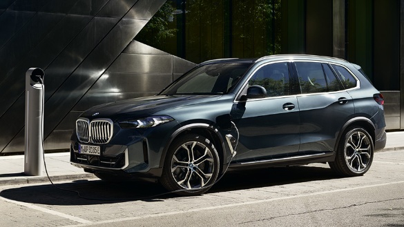 Ein dunkelblauer BMW X5 an einer Ladestation auf einem Parkplatz.