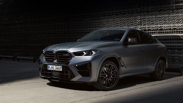 Gelber BMW X6 M in Seitenansicht vor einem metallischen Gebäude.