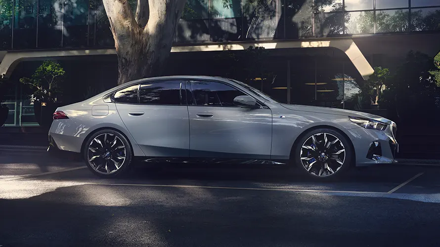 Silberner BMW in Seitenansicht, geparkt vor einem modernen Gebäude mit Bäumen.