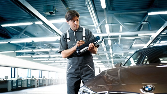 Mechaniker in Werkstatt mit BMW, hält ein Werkzeug in der Hand, Auto im Vordergrund.