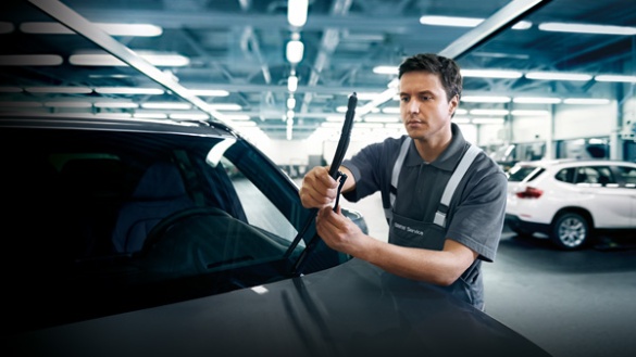 Ein Mechaniker wechselt Scheibenwischer an einem Auto in einer Werkstatt.