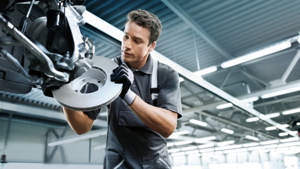 Mechaniker in Werkstatt montiert Bremsscheibe an einem Fahrzeug.