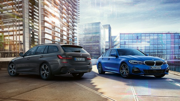 Zwei BMW 3er-Modelle, grau und blau, parken vor modernen Gebäuden.