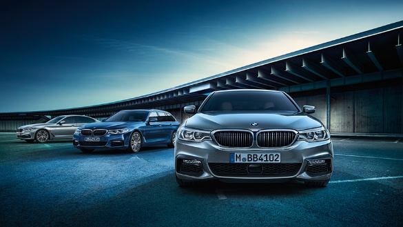 Drei silberne BMW-Limousinen auf einem Parkplatz, blauer Himmel im Hintergrund.