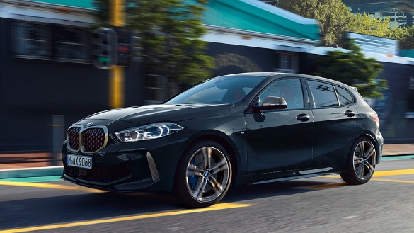 Ein schwarzer BMW 1er fährt auf einer Straße in städtischem Umfeld.