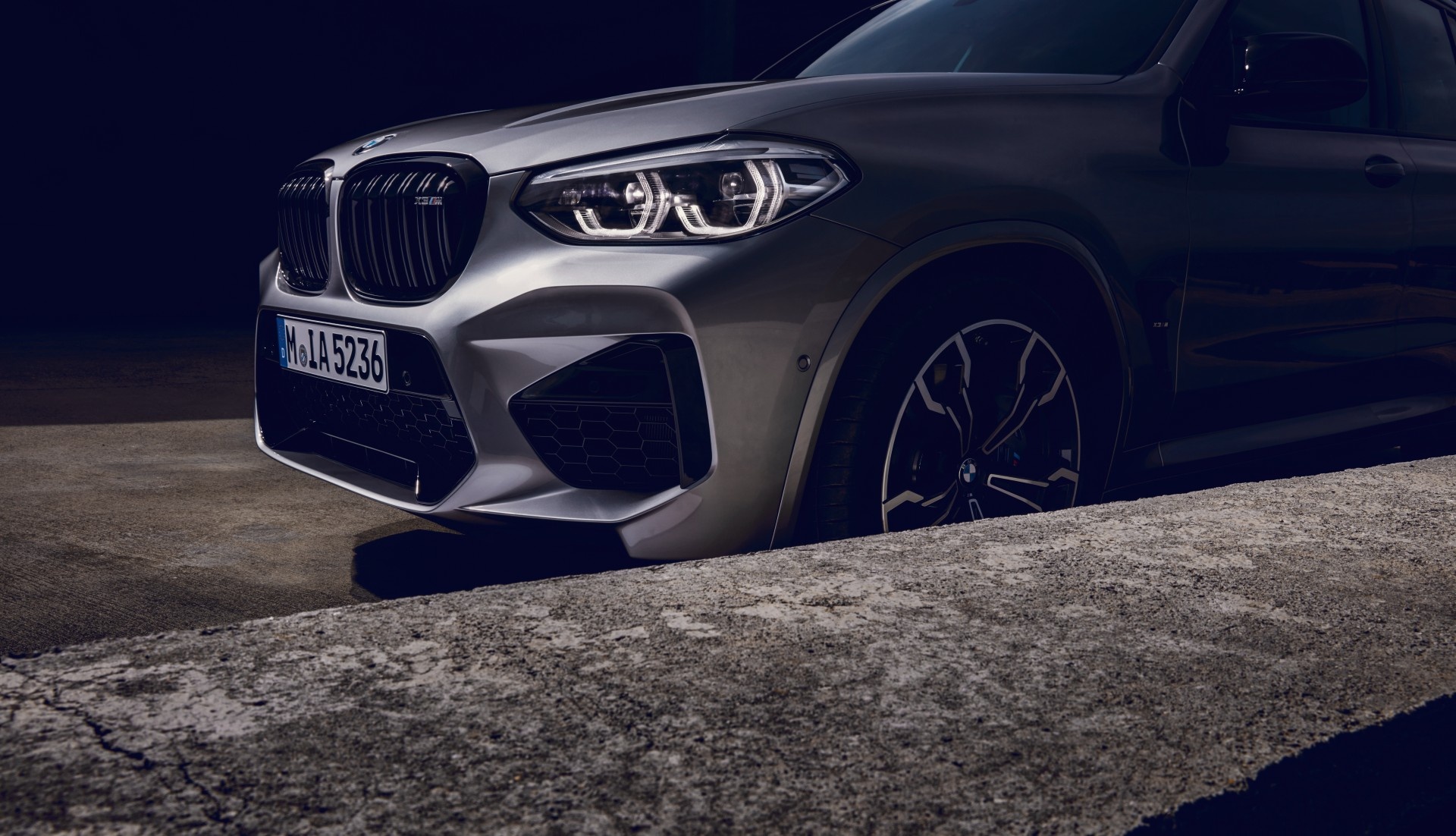 Silberner BMW X3 M mit Scheinwerfern und Nieren in Nahaufnahme, Nummernschild sichtbar.