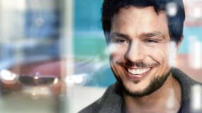 Lächelnder Mann vor verschwommenem Hintergrund mit Auto.