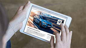 Person hält Tablet mit BMW-Werbung, blauer BMW auf dem Bildschirm.