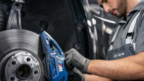 Mechaniker arbeitet an blauer BMW M Bremsanlage in Werkstatt.