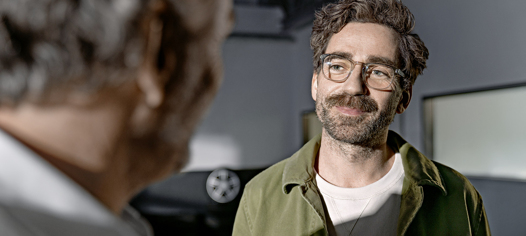 Zwei Männer im Gespräch, einer im Vordergrund unscharf, der andere lächelt und trägt eine Brille.