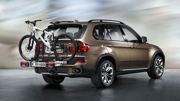Brauner BMW SUV mit Fahrradträger und Fahrrad auf grauem Hintergrund.