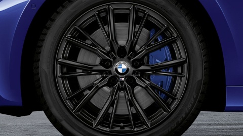 Nahaufnahme eines schwarzen BMW-Leichtmetallrads mit blauem Bremssattel auf grauem Hintergrund.
