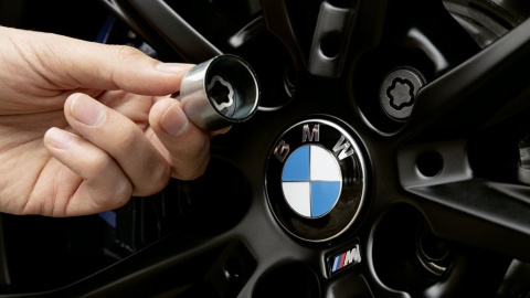 Hand hält eine Radschraubensicherung vor einem BMW-Rad mit Logo.