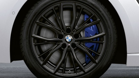 Nahaufnahme eines schwarzen BMW-Rades mit blauem Bremssattel auf grauem Hintergrund.
