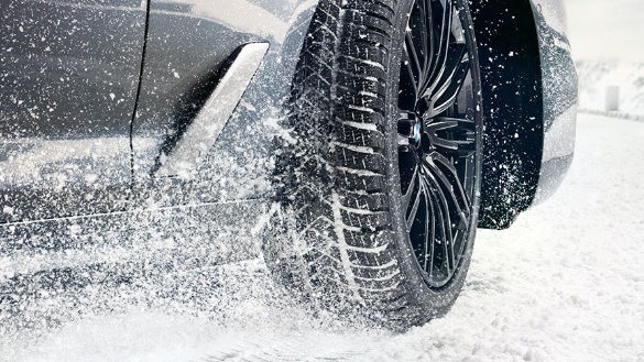 Nahaufnahme eines BMW-Reifen auf schneebedecktem Boden, Schnee spritzt auf.