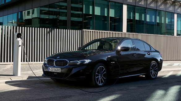 Schwarzer BMW 3er an Ladesäule vor modernem Gebäude, seitlich fotografiert.