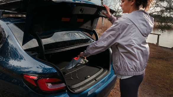 Person legt Sportschuhe in den Kofferraum eines blauen BMW SUV.