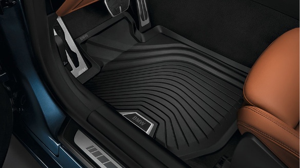 Schwarze BMW-Fußmatte im Autoinnenraum, neben braunem Ledersitz.