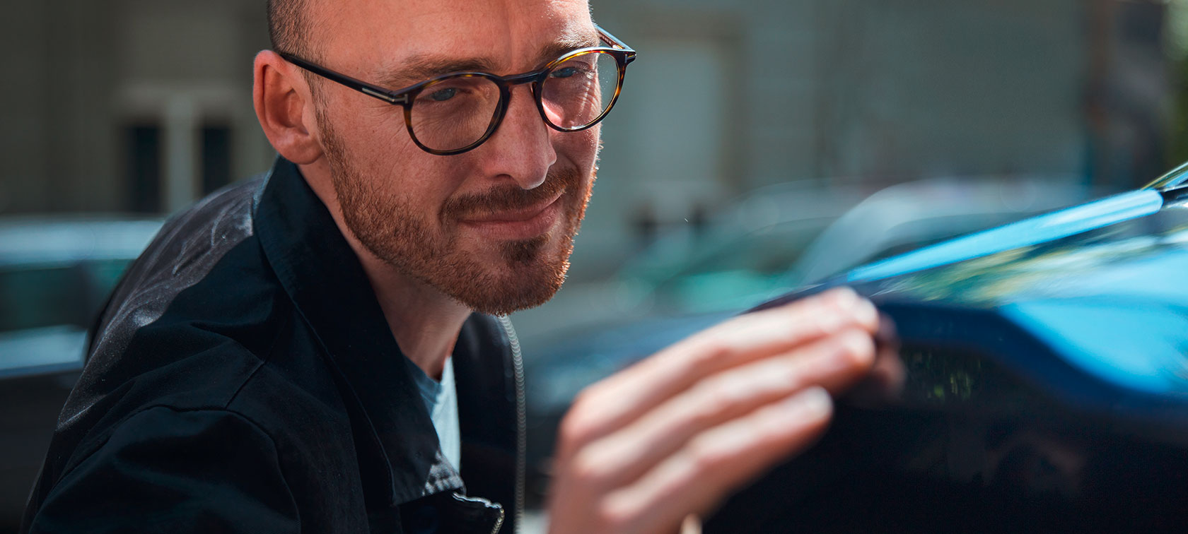 Mann mit Brille berührt ein blaues Auto im Freien.