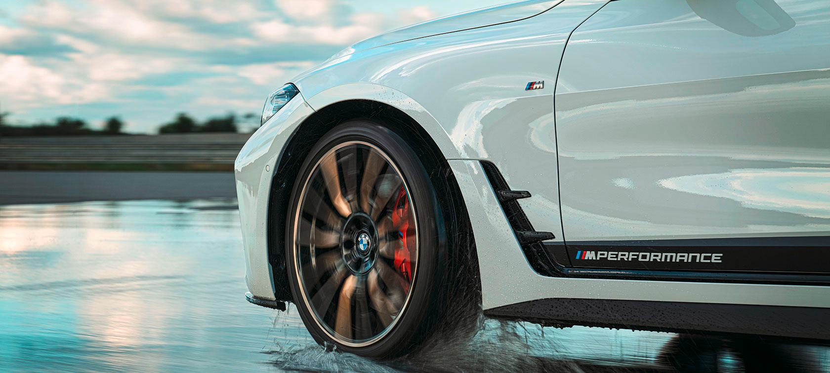 Nahaufnahme eines weißen BMW-Autos mit M-Logo auf nasser Fahrbahn.