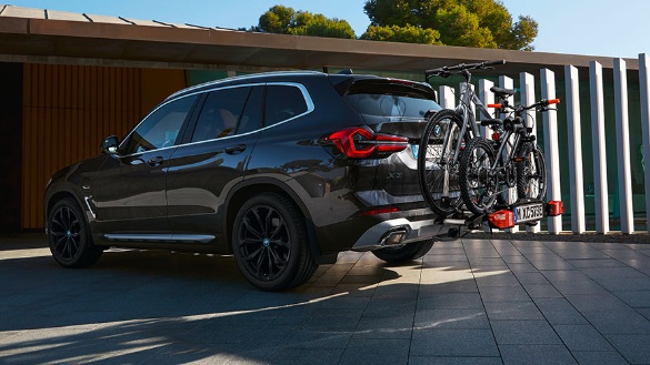 Schwarzer BMW SUV mit Fahrradträger und zwei Fahrrädern, geparkt vor modernem Gebäude.