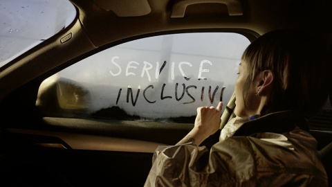 Eine Person schreibt "Service Inclusive" auf ein beschlagenes Autofenster.
