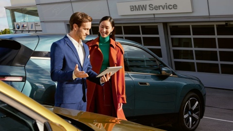 Ein Mann und eine Frau stehen vor einem BMW, Mann hält ein Tablet.