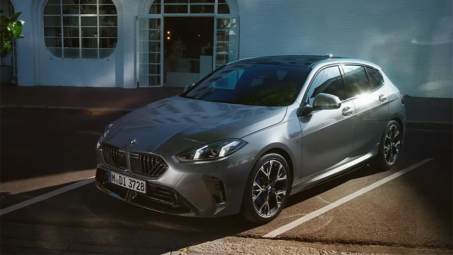Silberner BMW auf einer Straße vor einem weißen Gebäude, sonniges Wetter.