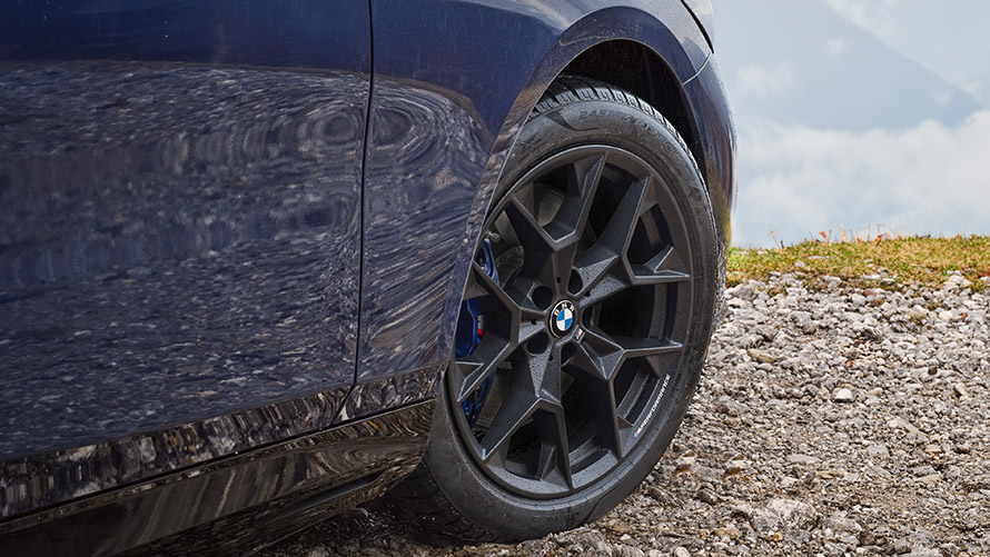 Nahaufnahme eines dunkelblauen BMW mit schwarzem Felgendesign auf einer Schotterstraße.