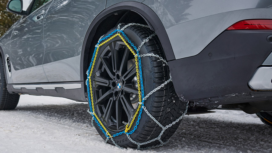 Nahaufnahme eines BMW-Reifens mit Schneeketten auf verschneitem Untergrund.