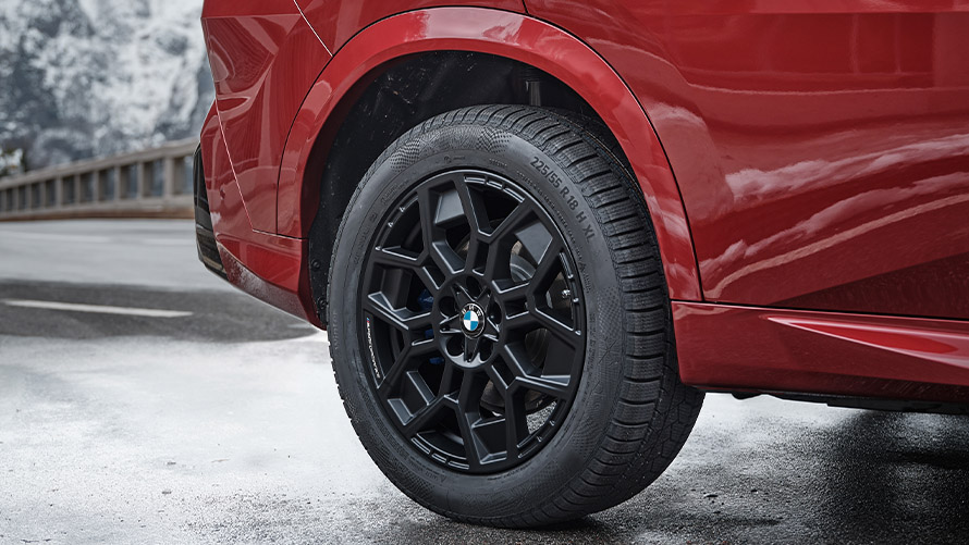 Roter BMW mit schwarzem Rad auf verschneiter Straße, Berglandschaft im Hintergrund.