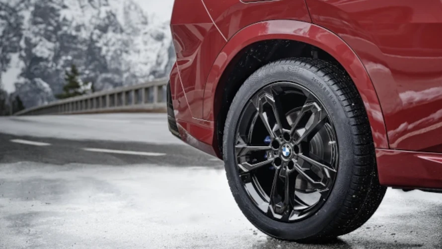 Rotes BMW-Auto auf verschneiter Straße, Fokus auf Hinterreifen; verschneite Berge im Hintergrund.
