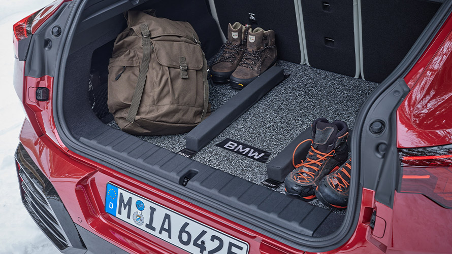 Roter BMW-Kofferraum mit Rucksack, Wanderschuhen und BMW-Logo auf grauem Teppich.