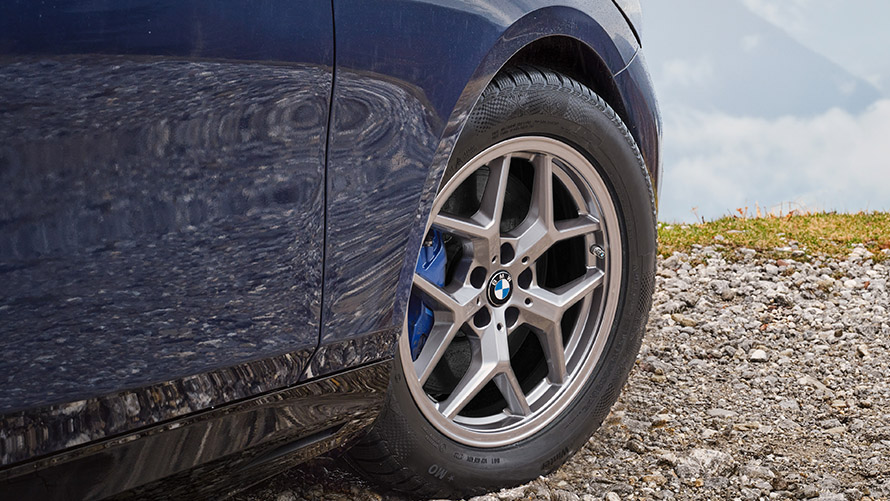 Nahaufnahme eines blauen BMW mit silberner Felge und blauem Bremssattel auf Schotterweg.