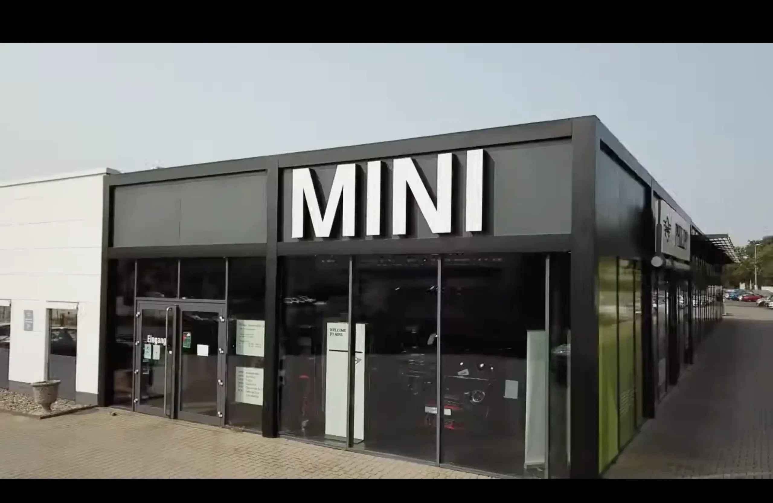 Gebäude mit MINI-Logo, Glasfassade, Eingangstüren, grauer Himmel.