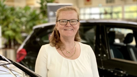 Eine lächelnde Person im Autohaus neben einem schwarzen Auto.