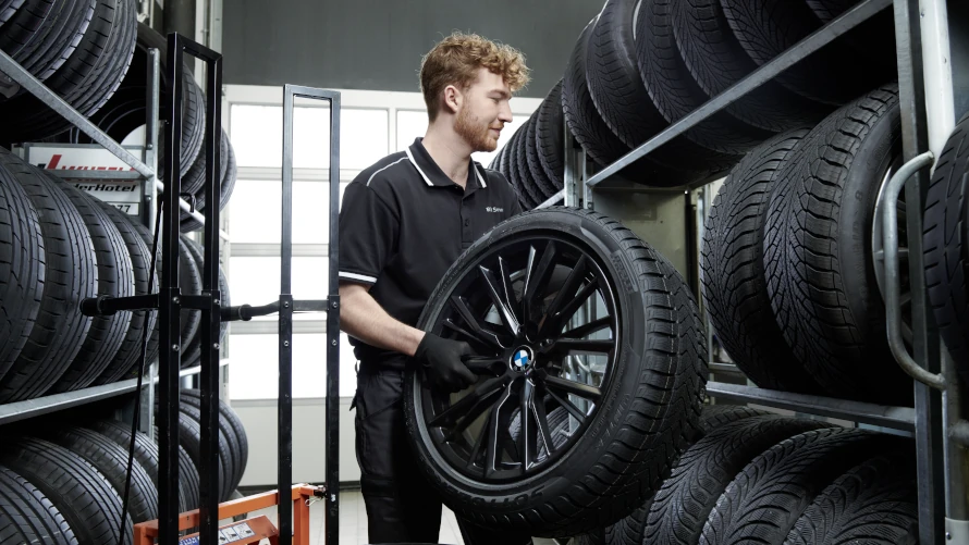 Mann in schwarzer Arbeitskleidung lagert BMW-Reifen in einem Regal ein.