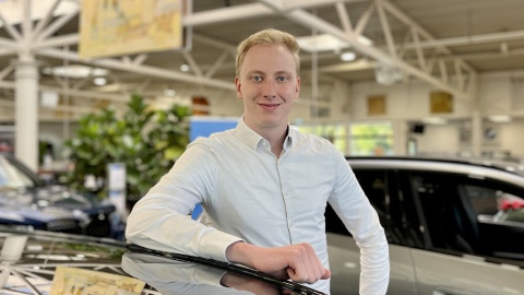 Eine Person in hellem Hemd steht in einem Autohaus neben einem schwarzen Auto.