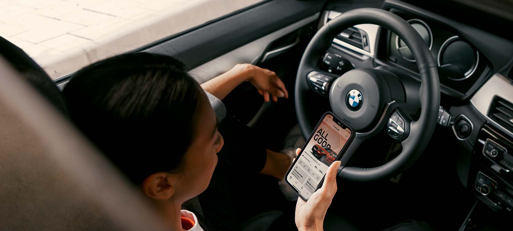 Person im Auto hält Smartphone, BMW-Lenkrad sichtbar.