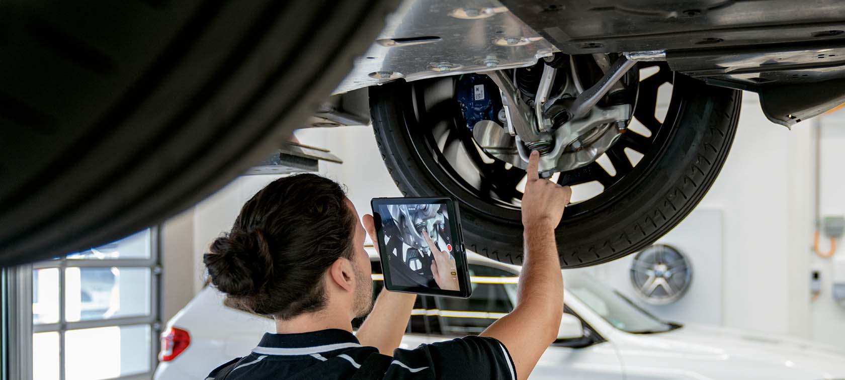 Mechaniker mit Tablet inspiziert ein angehobenes Fahrzeugrad in einer Werkstatt.