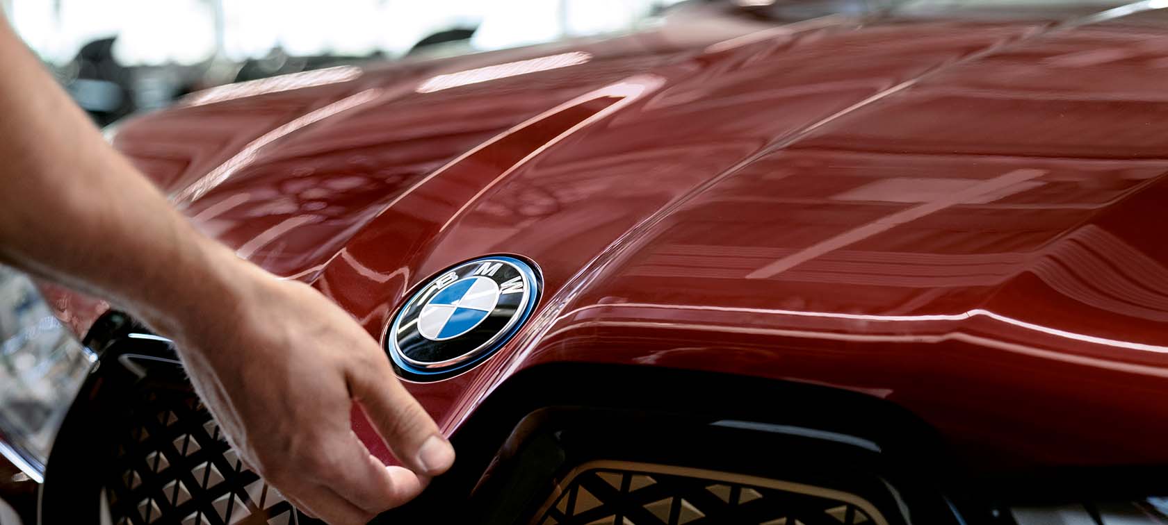 Rote BMW-Motorhaube mit Logo, Hand berührt den vorderen Teil in einer Werkstattumgebung.