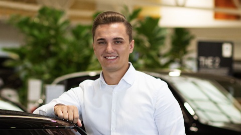 Ein Mann in weißem Hemd lehnt an einem schwarzen Auto in einem Autohaus.