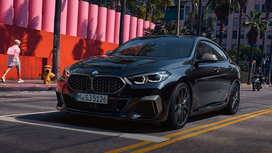 Schwarzes BMW 2er Gran Coupé auf Stadtstraße mit Palmen, im Hintergrund rosa Mauer.